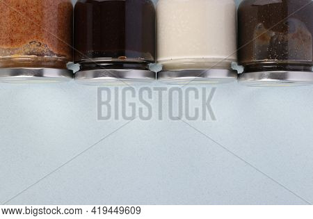 Vegan Organic Paste Of Flax Seeds, Milk Thistle, Peanuts And Coconut In Glass Jars On Light Blue Bac