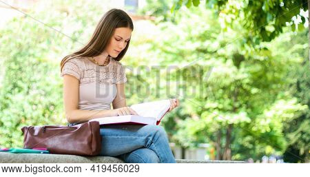 Beautiful female college student reading a book on a bench in a park