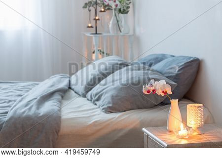 Orched Flowers  In Vase And Burning Candles In White Bedroom