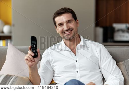 Front Image Of A Handsome Smiling Man Looking At Cameraa Holding In Hands A Stationary Phone Sitting