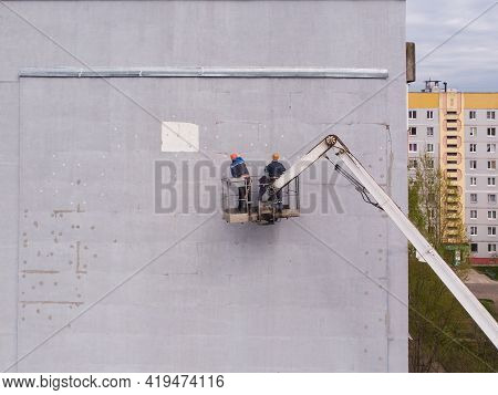 Two Workers Stand On Aerial Platform And Insulate The Wall Of The House