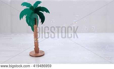 Rtificial Palm Tree And Rainbow Soap Bubbles On A White Wooden Table. Relaxation And Imagination Con