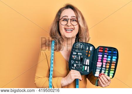 Middle age caucasian woman wearing tape measure holding sew kit smiling and laughing hard out loud because funny crazy joke. 