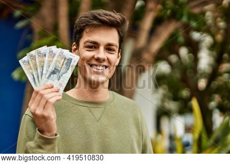 Young hispanic man smiling happy holding peruvian soles banknotes at the city.