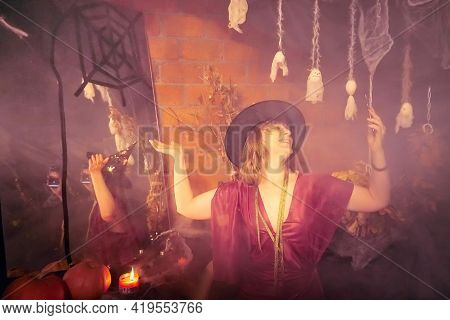 Blonde Witch In Red Dress And Black Hat With Candle And Mirror In Halloween Decoration Indoors.