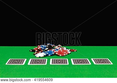 Poker Chips On A Gaming Table In A Casino With Dramatic Lighting. Green Table And Black Night Backgr
