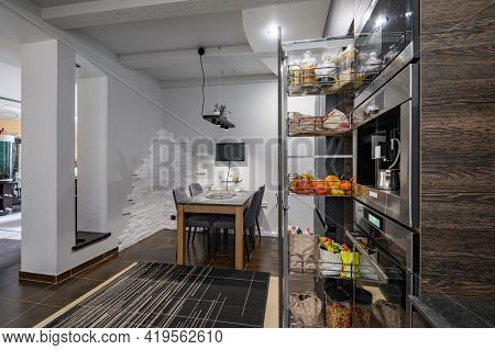 Modern large luxurious dark brown kitchen showcase interior, with dining table showing big vertical drawer with storage compartment pulled out