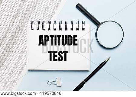 On A Light Blue Background, Reports, A Magnifying Glass, A Pen And A Notebook With The Text Aptitude