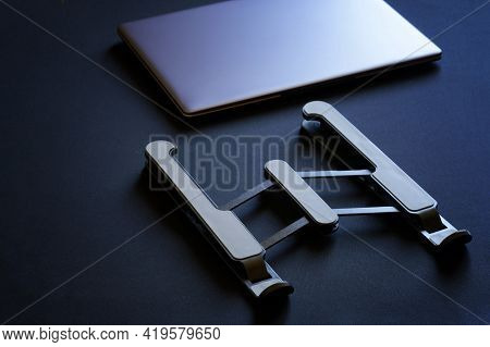 The Portable Foldable Laptop Stand Lies On A Dark Surface Next To A Closed Laptop Or Ultrabook. The 