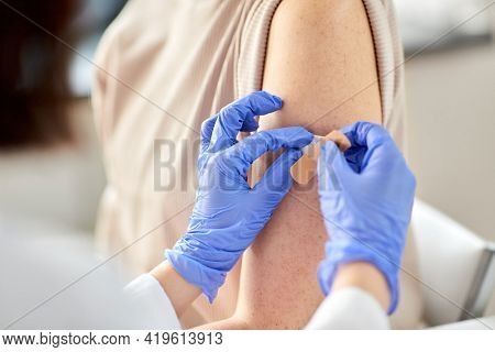 health, medicine and vaccination concept - close up of doctor attatching adhesive medical plaster or patch to patient at hospital