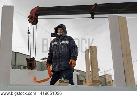 A Portrait Of A Fitter In A Blue Jacket At The Hook Of A Truck Crane