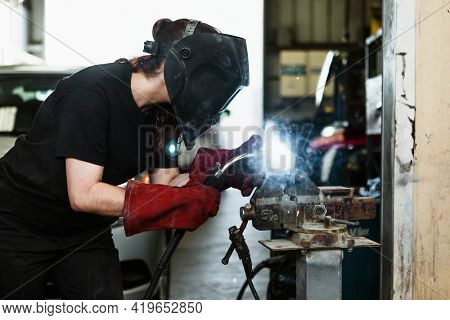 Female welding a metal piece in the garage