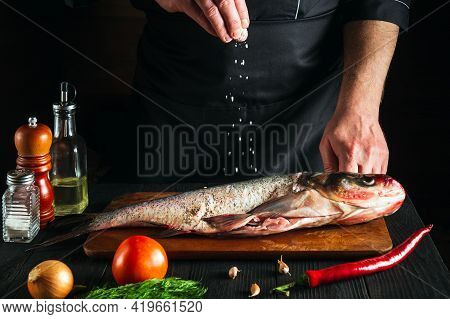 Chef Or Cook Prepares Fresh Fish Bighead Carp Sprinkling Salt With The Ingredients. Preparing To Coo