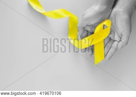 Hand Holding Yellow Ribbon On Green Background, Copy Space. Bone Cancer Sarcoma Awareness Childhood 