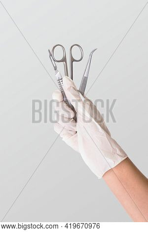 Gloved hand holding stainless steel medical instruments