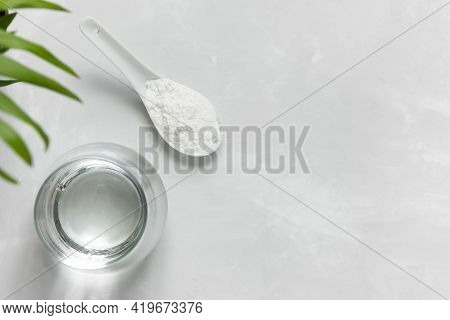 Collagen Powder In A Spoon And A Glass Of Water On A Gray Concrete Background With A Copy Space. Ext