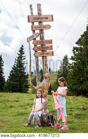 Children In Front wooden Signpost On Velika Planina In Slovenia.