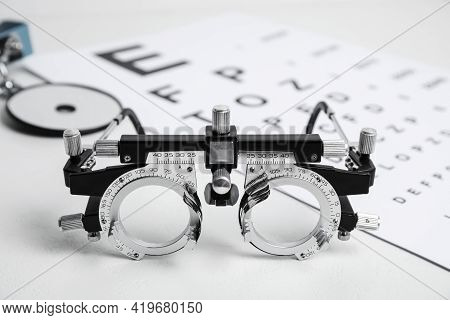 Trial Frame, Head Mirror And Eye Chart Test On White Table. Ophthalmologist Equipment