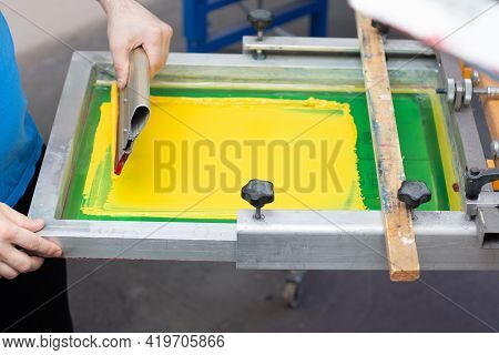Serigraphy Silk Screen Print Process At Clothes Factory. Frame, Squeegee And Plastisol Yellow Color 