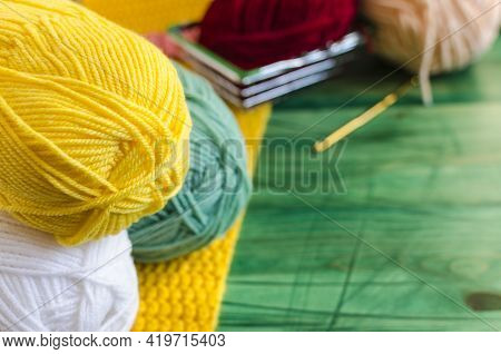Skeins Of Colored Yarn In The Foreground And Knitting With A Metal Basket In The Background, Blurred