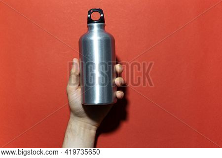 Close-up Of Male Hand Holding Reusable Aluminum Thermo Water Bottle On Background Of Red Textured Wa