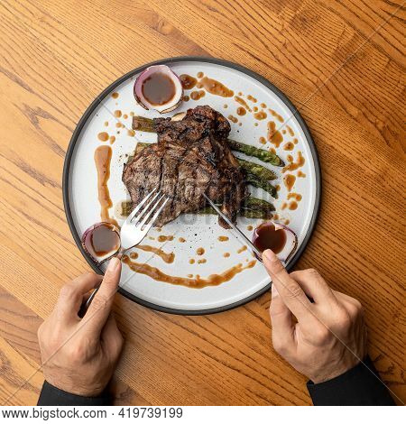 Male Hands With Knife, Fork And Food Plate With Juicy Grilled Steak. Man Having Lunch In Restaurant.