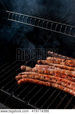Roasted Bbq Sausages With Grillmarks Cooking On Grill Barbecue With Smoke. Outdoor Summertime Meal P