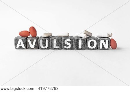 Avulsion The Word On Stone Cubes. Cubes Stand On A White Surface, Many White And Red Pills. Medicine
