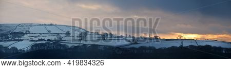 Panoramic View Of A Glowing Orange Sunset In A Cloudy Twilight Winter Sky With Snow Covered Fields W