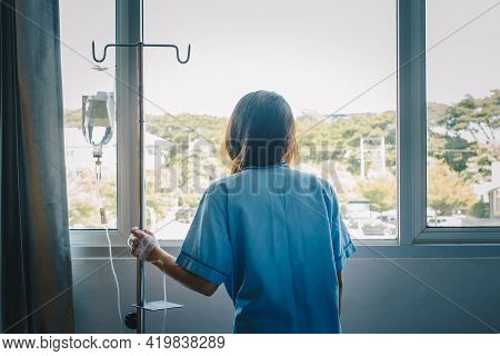 Back View Of Sickness Patient Woman Standing Nearly Window In Hospital Ward, Looking To Outside And 