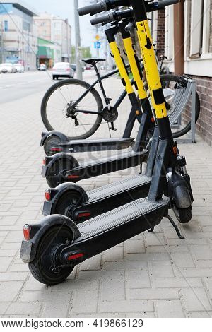 Scooters And Bicycles In A Parking Lot In The City. The Concept Of Modern Transport