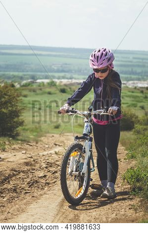 Konstantinovka, Ukraine - May 8, 2021: Tired Little Girl With A Bicycle Walks Up The Hill