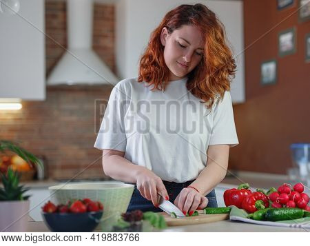 Beautiful Redhair Young Woman Is Preparing Vegetable Salad In The Kitchen.