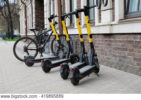 Scooters And Bicycles In A Parking Lot In The City. The Concept Of Modern Transport