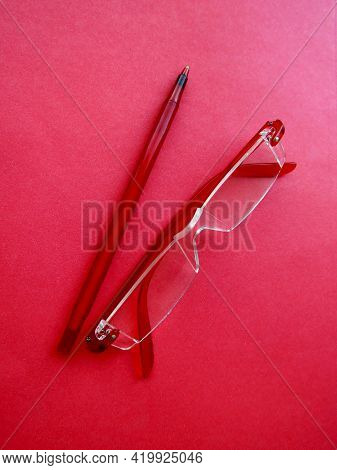 Red Rimless Reading Eyeglasses And Red Pen On Red Paper Background