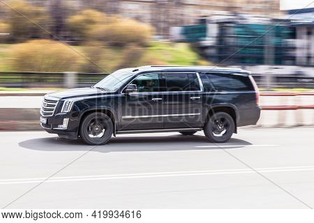 Side View Rolling Shot With Black Suv Car In Motion. Cadillac Escalade Esv Driving Along The Street 