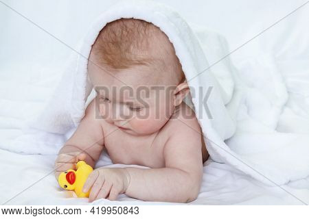 A Wet Baby Covered With A White Towel Dries Up After Bathing And Plays With A Toy. Copy Space - The 