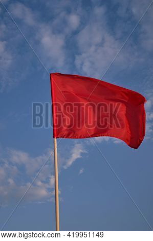 Red Flag With Blue Sky With Clouds, Strong Wind Flying Red Flag. Red Flag Warning Flags