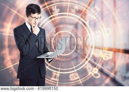 Businessman Holding A Laptop And Thinking In An Office Corridor With A Circle With Zodiac Signs, Pre