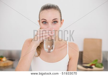 Happy young woman drinking glass of water in the kitchen at home