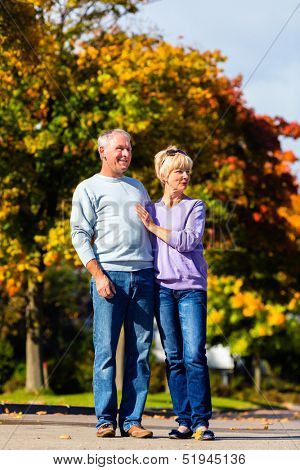 senior couple, Man and woman, having a walk in autumn or fall outdoors, the trees show colorful foliage