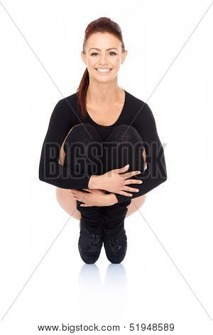 Smiling woman balancing on her toes while crouching down hugging her bended knees during a workout and training exercises  on a white background