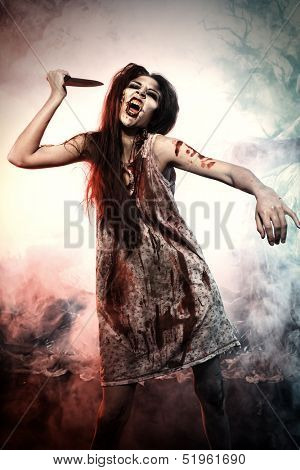 Bloodthirsty zombi with a knife standing at the night cemetery in the mist and moonlight.