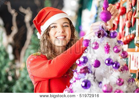 Portrait of happy beautiful female owner decorating Christmas tree in store