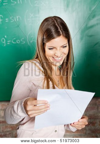 Happy female student looking at exam result against greenboard in classroom