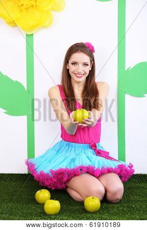 Beautiful young woman in petty skirt with apples on decorative background
