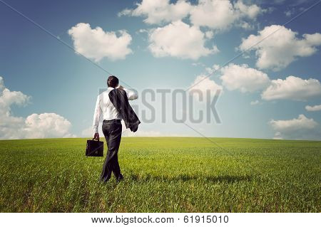 Businessman In A Suit Walking On A Spacious Green Field With A Blue Sky