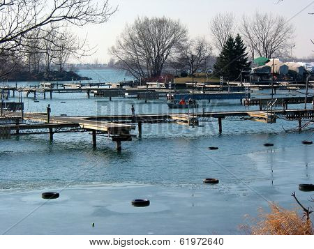 Sailboats drydocked next to the docks in a harbor on half frozen lake