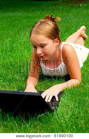 Young girl lying on grass in a park with laptop computer