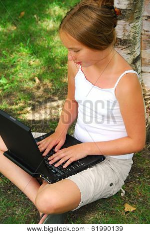 Young girl sitting in a park with laptop computer